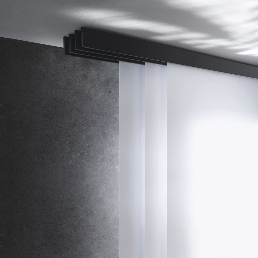 Puristisches Interstil Flächenvorhang-System „F1“ in mattem Schwarz bei der Deckenmontage. Das Bild zeigt eine mehrläufige, flache Aluminiumschiene, in der drei weiße, halbtransparente Stoffpaneele linear hintereinander geführt werden. Das Design ist extrem reduziert und schließt bündig mit der Decke ab, kombiniert mit einer dunklen Wand in Sichtbeton-Optik.
