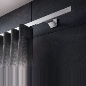 Nahaufnahme des Interstil Vorhangschienensystems „Index“. Eine flache, minimalistische Vorhangschiene aus hochwertigem, matt gebürstetem Aluminium, die mit einem eckigen Wandhalter montiert ist. An der Schiene hängt ein heller Wellenvorhang mit einer dezenten Netzstruktur. Das Design wirkt modern und geradlinig.